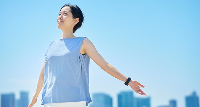 トレーニングウェアを着た女性が青空の下で気持ち良さそうに手を広げる様子